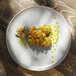 A Corona by GET Enterprises Cosmos porcelain plate with food on it on a wood table.