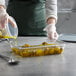 A person in gloves pouring olive oil into a Vigor clear plastic food pan.