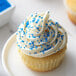 A cupcake with white frosting and Blue Nonpareils sprinkles.