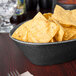 A black oval basket filled with chips on a table.