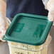 A person in gloves holding a Vigor square green polypropylene food storage container filled with shredded cheese.