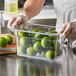 A person in gloves holding a Vigor clear polycarbonate food pan full of limes.