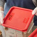 A person in gloves holding a red Vigor polypropylene food storage container with food.
