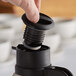 A hand using a black and silver Twist Lid to pour coffee into a coffee carafe.