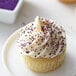 A cupcake with white frosting and purple nonpareils.