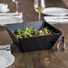 A black square melamine bowl filled with salad on a table.