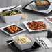 A table with a variety of dishes including a black Acopa Rittenhouse melamine bowl filled with rice and vegetables.
