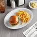 An Acopa white melamine oval platter with a burger and fries and a glass of soda on it.