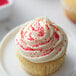 A close up of a cupcake with white frosting and pink sprinkles.
