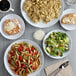 A table with plates of pasta, salad, and bread on Acopa Lunar white melamine plates.