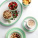 A table set with a plate of fruit and nuts, a bowl of cereal, and a green porcelain stackable soup cup filled with coffee.