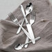 A Fortessa Grand City stainless steel serving spoon next to a knife on a table with silverware.