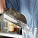 A person using a Tablecraft stainless steel ice scoop to pour ice into a glass.
