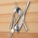 A Fortessa Lucca stainless steel serving fork on a wood surface with silverware.