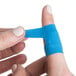 A person using a San Jamar Mani-Kare blue knuckle bandage on a finger.