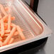 French fries in a black pan under a heat lamp on a countertop.