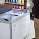 A man holding a cup of ice cream in an Avantco flat top display freezer.