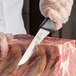 A person using a Mercer Culinary stiff boning knife to cut meat.