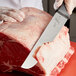 A person cutting meat with a Mercer Culinary European Butcher Knife.