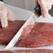 A person using a Mercer Butcher knife to cut meat.