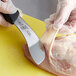 A person in gloves using a Mercer Culinary skinning knife to cut meat on a cutting board.