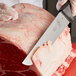 A person using a Mercer Culinary European Butcher Knife to cut meat on a counter.