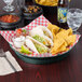 A table with a plate of tacos, chips, and a 12" round polypropylene server filled with jalapenos.