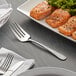 An Acopa stainless steel serving fork on a plate of salmon and broccoli.