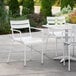 A white Lancaster Table & Seating outdoor arm chair on a patio.