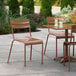 A Lancaster Table & Seating brown powder coated aluminum outdoor side chair on a patio with drinks on the table.