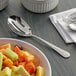 An Acopa stainless steel slotted serving spoon next to a bowl of fruit.