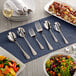 An Acopa stainless steel slotted serving spoon on a table set with plates and silverware.