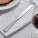 An Acopa stainless steel dinner knife on a napkin next to a plate of meat.