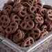 A plastic container of Micro Mini Cocoa Pretzels with a pile of chocolate covered pretzels.