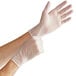 A pair of hands wearing Noble Products clear vinyl gloves.