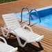 Two white Lancaster Table & Seating adjustable resin chaise lounges next to a pool.