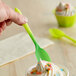 A hand holding a neon green spoon over a cup of ice cream.