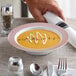 A Visions white plastic bowl filled with soup on a table with a spoon.