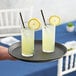 A black Choice non-skid serving tray holding two glasses of lemonade with straws and lemon slices.