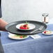 A person holding a Choice black round non-skid serving tray with a plate of dessert with berries on it.