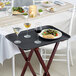 A Choice black non-skid serving tray with food and wine glasses on it.