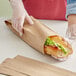 A hand in a glove holding a Choice Kraft paper bag with a submarine sandwich inside.