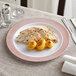 A Visions white plastic plate with rose gold lattice design holding chicken and potatoes on a table.
