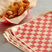 A basket of fried onion rings next to red checkered deli wrap paper.