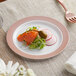 A Visions white plastic plate with a rose gold lattice design holding food on a table.