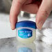 A hand holding a small blue jar of Vaseline Lip Therapy.