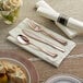 A Visions white pre-rolled napkin with rose gold plastic cutlery including a fork and knife on a napkin.
