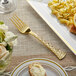 A Visions gold plastic fork on a white plate with pasta and lemon slices.