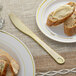 A Visions heavy weight gold plastic knife next to a piece of bread with butter on a plate.