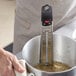 A hand uses a Cooper-Atkins candy/deep fry paddle thermometer in a pot of liquid.
